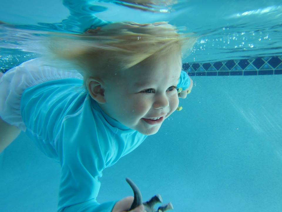 infant swimming with toy in hand